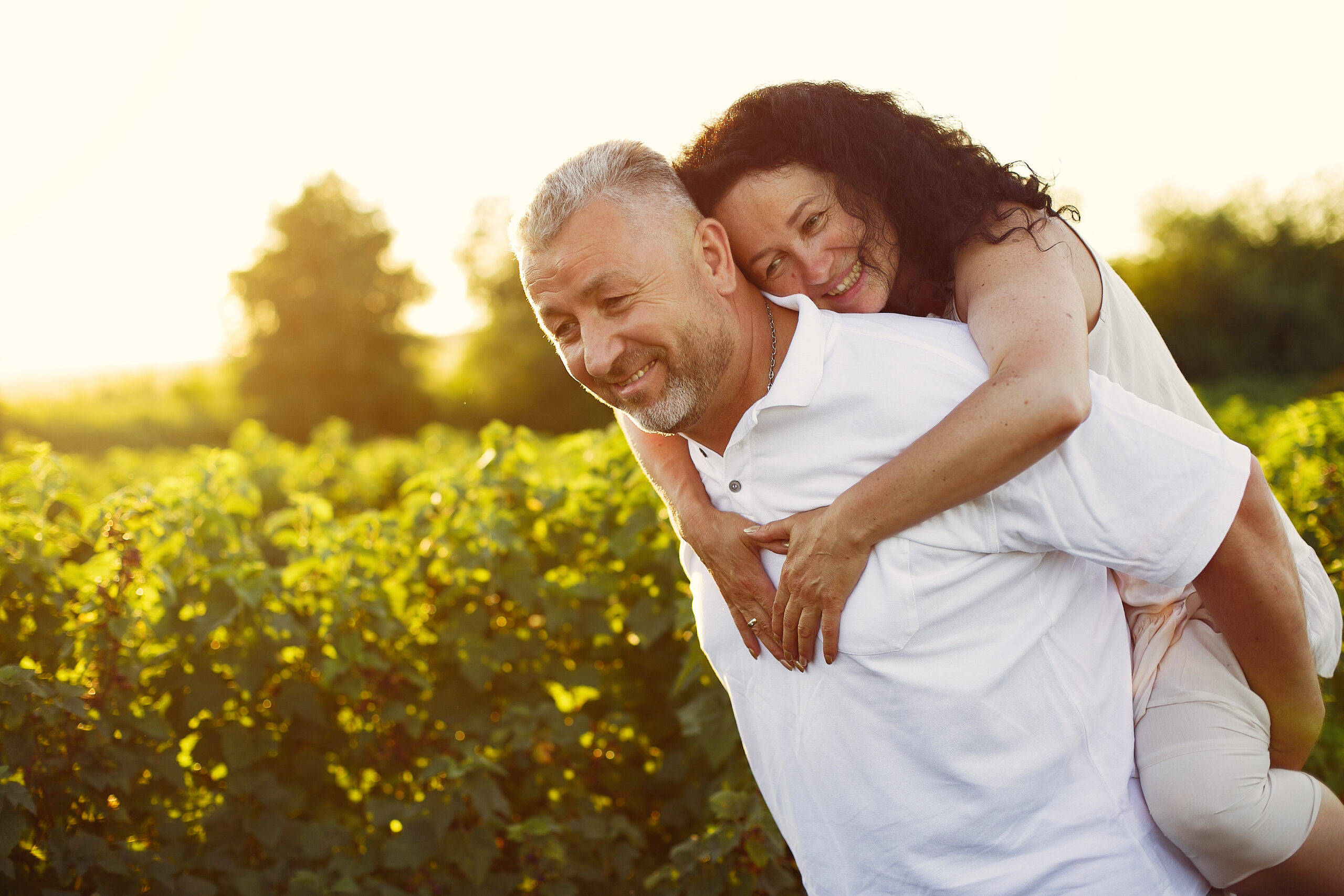 Aduld couple in a summer field. Handsome senior in a white shirt. Woman in a white dress